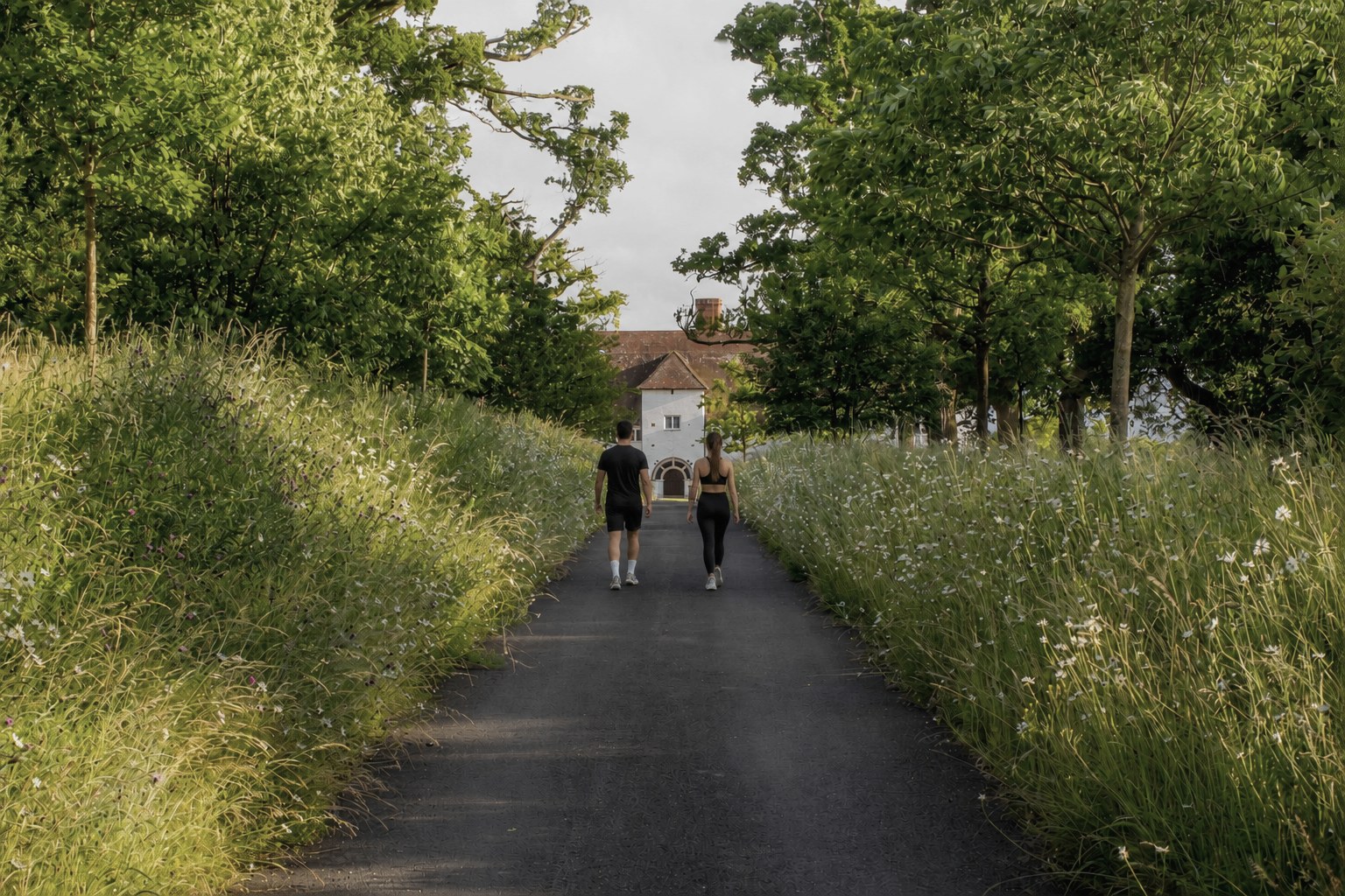 Two people walking down a tree-lined avenue toward the Marshcourt estate at dusk